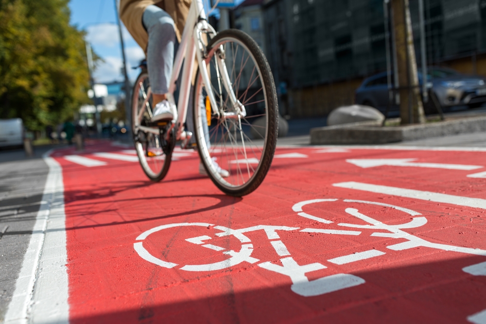 Cyclist riding in a designated red bike lane with white bicycle symbol on an urban city street for safe cycling transportation.