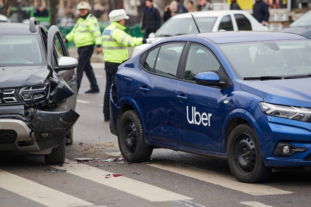 Uber car accident with another vehicle on city street, showing damaged cars and police officers at the crash scene. Uber car accident with another vehicle on city street, showing damaged cars and police officers at the crash scene.