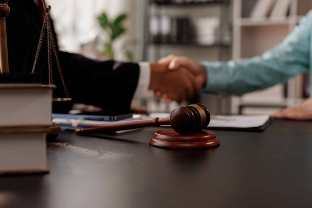 Lawyer and client shaking hands in an office with gavel and legal documents on the desk.