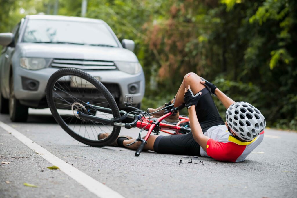Injured cyclist lying on the road after bicycle accident with SUV, holding knee in pain while wearing helmet and protective gear. Injured cyclist lying on the road after bicycle accident with SUV, holding knee in pain while wearing helmet and protective gear.