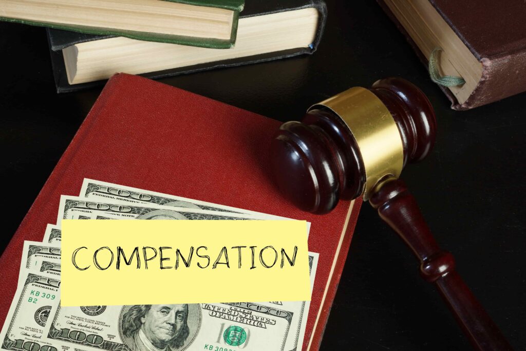 Judge&rsquo;s gavel resting on law books and US dollar bills with &ldquo;Compensation&rdquo; note, symbolizing legal settlement and financial damages award.