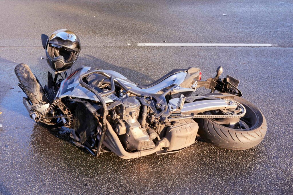 Damaged motorcycle lying on road after crash with helmet nearby, illustrating motorbike accident scene and road hazard