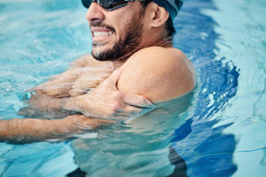 Man in swimming pool holding shoulder in pain, illustrating swimming injury, shoulder strain, and personal injury or sports-related accident.