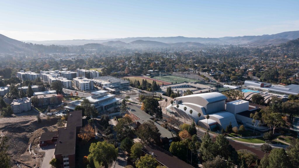 Aerial view of suburban cityscape with university campus buildings, sports fields, and surrounding hills under clear sky
