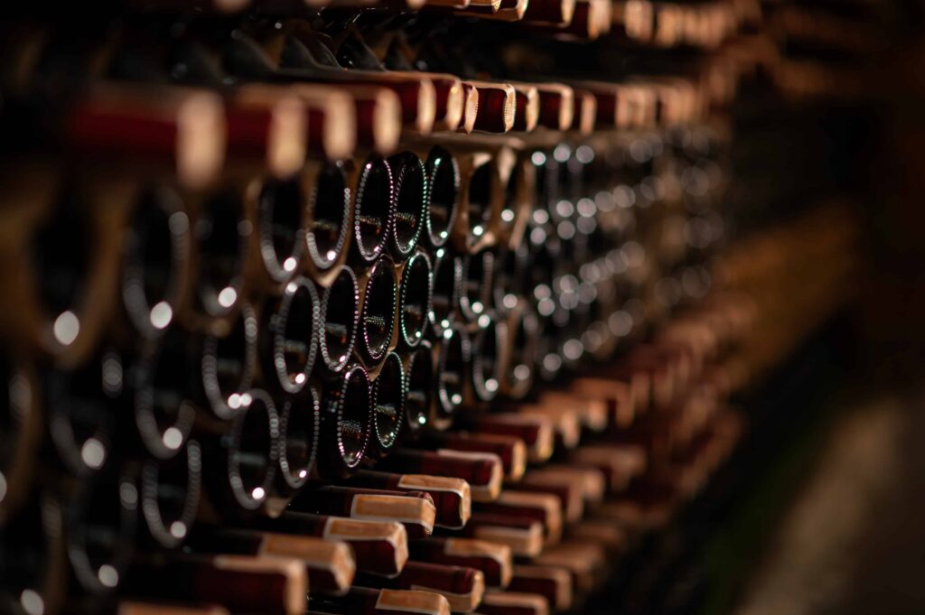 Rows of wine bottles stored horizontally in a dimly lit cellar, aging on wooden racks