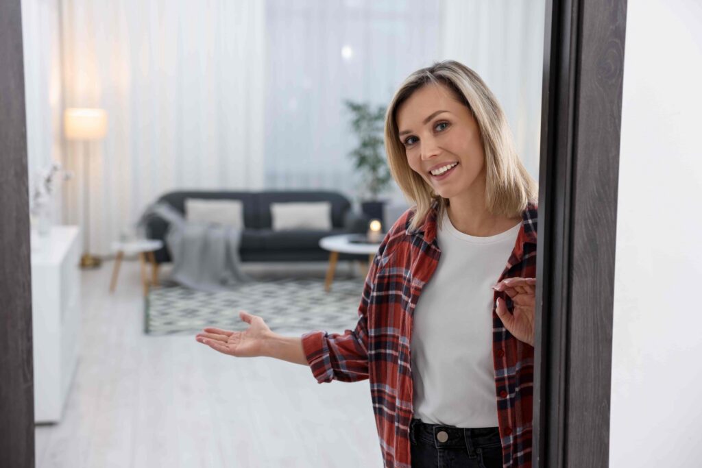 Woman welcoming guests at doorway into modern living room, showcasing home interior and hospitality in a residential setting.