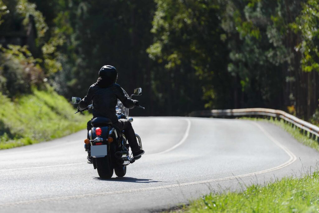 Motorcyclist riding on a winding scenic road through a forest, wearing helmet and protective gear Motorcyclist riding on a winding scenic road through a forest, wearing helmet and protective gear