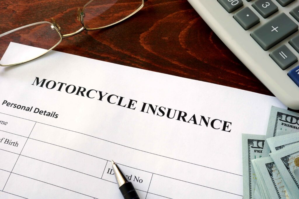 Motorcycle insurance application form on desk with calculator, glasses, pen, and cash, representing insurance coverage, policy costs, and financial planning.