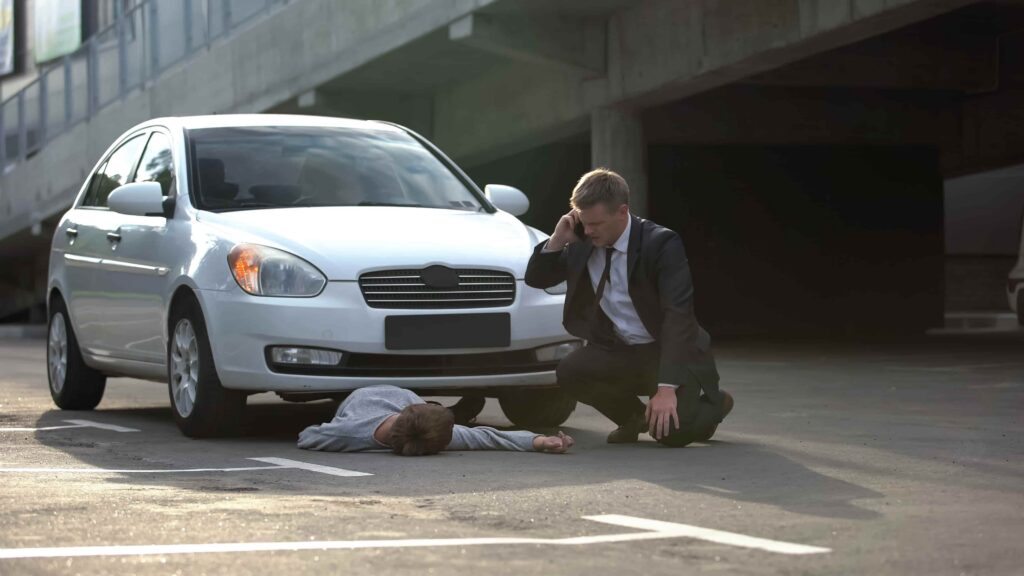 Pedestrian hit by car with injured person lying on road and driver calling for emergency assistance in parking area